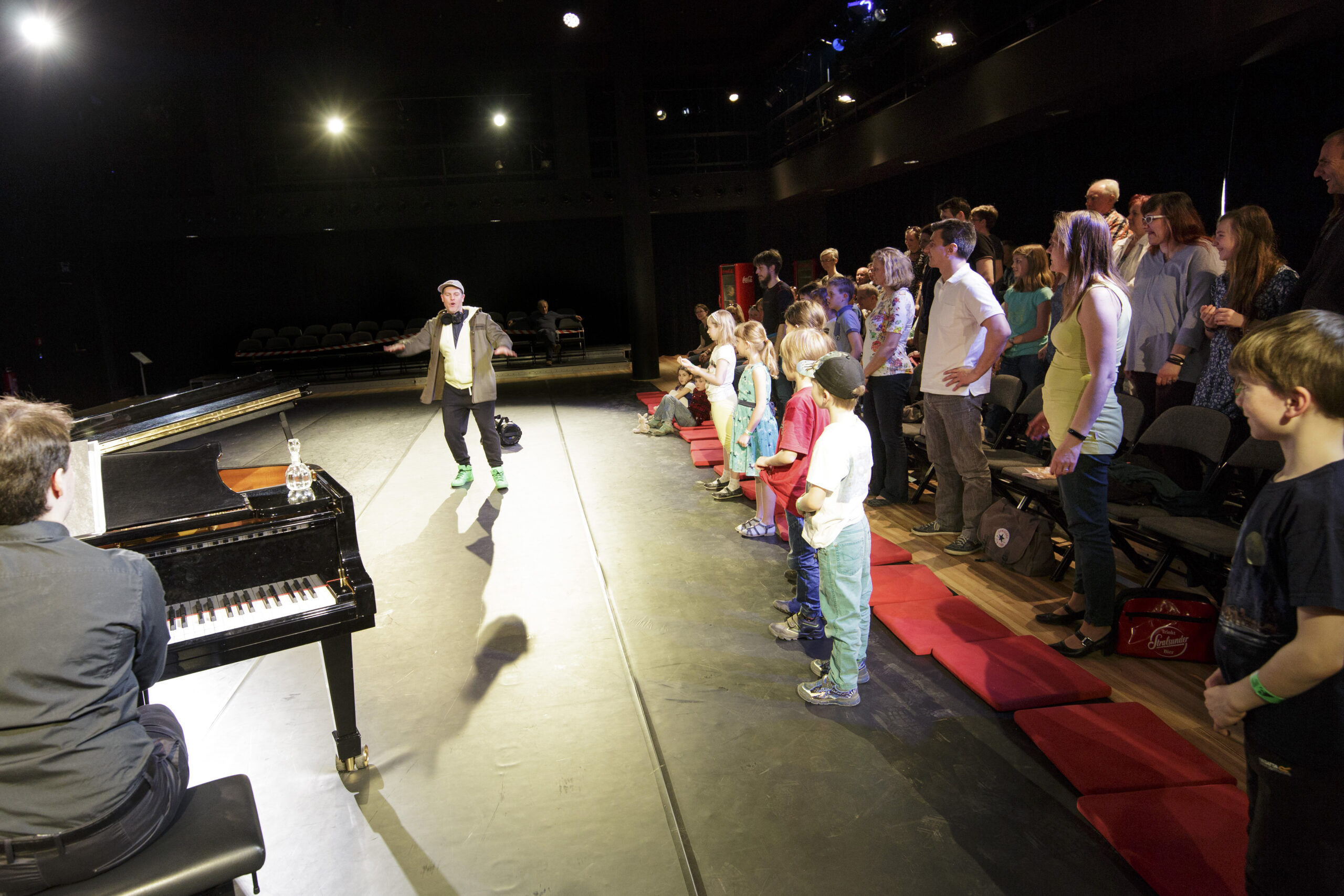 Ein Mann tanzt auf der Bühne. Kinder sehen zu. Links im Bild sieht man einen Klavierspieler.